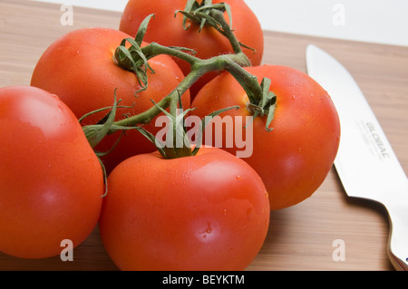 Organici di pomodori a grappolo con coltello da cucina in bambù tagliere Foto Stock