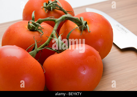 Organici di pomodori a grappolo con coltello da cucina in bambù tagliere Foto Stock