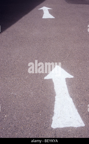 Due grandi frecce bianche in successione amateurishly dipinta su strada asfaltata superficie parzialmente in ombra Foto Stock