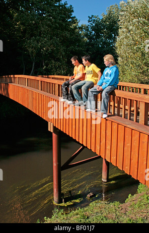 Tre ragazzi adolescenti seduti sulla staccionata di un ponte pedonale in un fiume Foto Stock