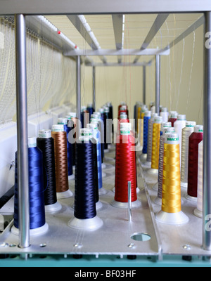 I thread in un arcobaleno di colori sono avvolti su bobine speciali per uso industriale su macchine da ricamo. Foto Stock