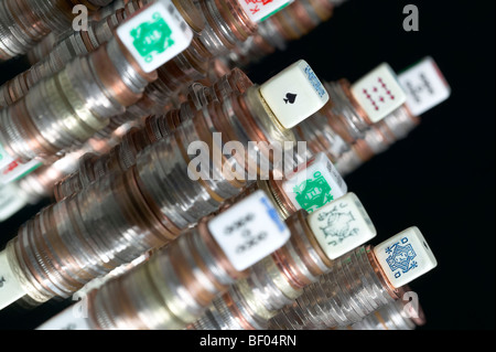 Studio shot di pile di monete con il poker di dadi sulla parte superiore di pile con sfondo nero girato di un angolo Foto Stock