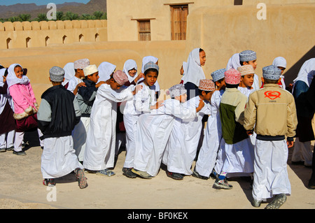 Insegnante femmina di un misto di classe scolastica di vivaci ragazzi e ragazze su una escursione nel castello di Nizwa, Sultanato di Oman Foto Stock