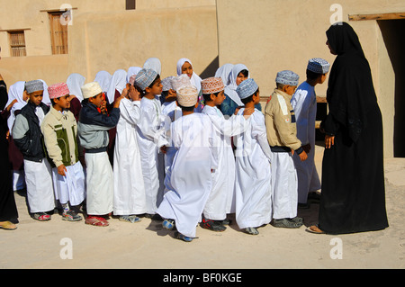 Insegnante femmina di un misto di classe scolastica di vivaci ragazzi e ragazze su una escursione nel castello di Nizwa, Sultanato di Oman Foto Stock