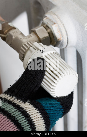 Una mano che indossa un guanto girando la manopola di un radiatore Foto Stock