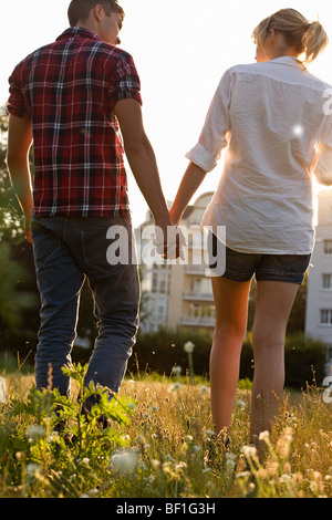 Una giovane coppia tenendo le mani a piedi attraverso un parco, vista posteriore Foto Stock