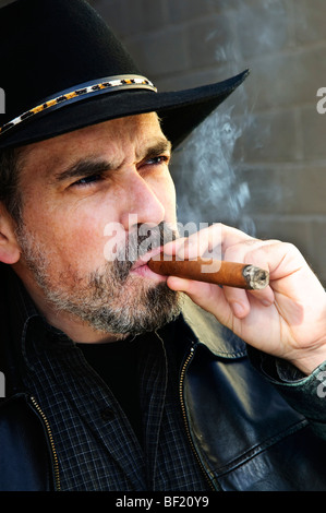 Uomo con la barba nel cappello da cowboy di fumare il sigaro Foto Stock