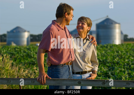 Il marito e la moglie gli agricoltori nel loro campo di soia di condividere alcuni momenti personali insieme con contenitori del cereale in background / STATI UNITI D'AMERICA. Foto Stock