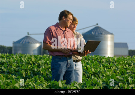 Il marito e la moglie gli agricoltori in piedi nel loro campo di soia in ingresso i dati di raccolto nel proprio computer portatile da un campo di GPS map / STATI UNITI D'AMERICA. Foto Stock