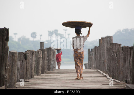 Due donne birmane, visto da dietro portando un cesto sulla loro testa mentre si cammina sulla U Beins ponte in Amarapura vicino a me Foto Stock