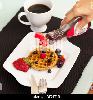 Close-up di una persona lo sciroppo di colata su cialde Foto Stock