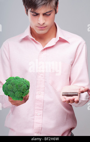 L'uomo scegliendo tra i broccoli e cioccolata Foto Stock