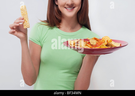 Donna scegliendo tra una proteina bar e un piatto di nachos Foto Stock