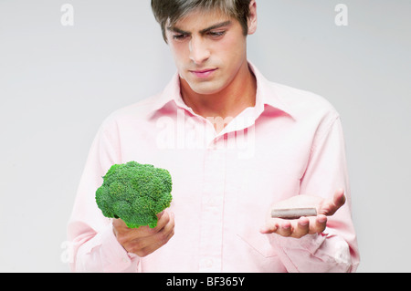 L'uomo scegliendo tra i broccoli e cioccolata Foto Stock
