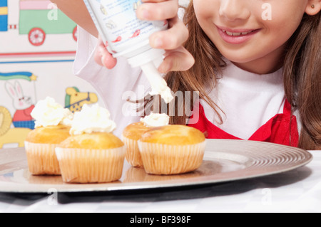 Ragazza di mettere la panna montata su tortine Foto Stock