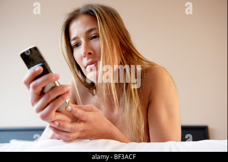Donna sul suo letto, con il cellulare Foto Stock