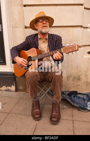 Un anziano uomo barbuto busker a suonare la chitarra musicista di strada a Norwich, Norfolk, Regno Unito Foto Stock