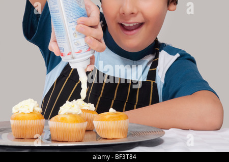 Close-up di un ragazzo di mettere la panna montata su tortine Foto Stock