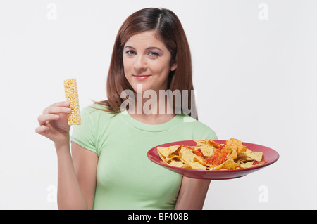 Donna scegliendo tra una proteina bar e un piatto di nachos Foto Stock