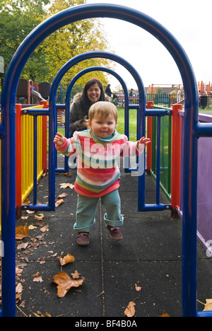 Ritratto verticale di una giovane madre a giocare con la sua bimba in corrispondenza di un elemento tubolare a labirinto in corrispondenza di una zona giochi per bambini. Foto Stock