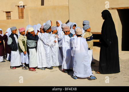 Insegnante con una classe mista di vivaci ragazzi e ragazze su una gita al Forte di Nizwa, Sultanato di Oman, medio Foto Stock