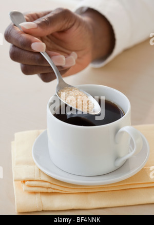 Donna africana di mettere lo zucchero nel caffè Foto Stock