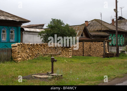 Legna da ardere impilati e acqua di comunità toccate da case in città rurale, Ural, Russia Foto Stock