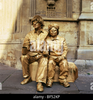 Intrattenitori di strada dipinti d'oro statue viventi con bicchieri da collezione di monete vicino alla Cattedrale di Bath, Bath, Inghilterra Regno Unito Gran Bretagna KATHY DEWITT Foto Stock