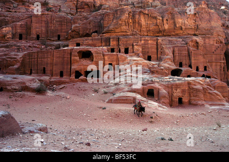 Un beduino cavalca il suo cavallo davanti alle tombe sulla strada delle facciate, Petra, Giordania Foto Stock