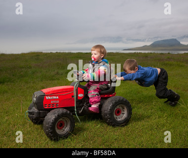 Ragazzo giovane spingendo la sua sorella più giovane sul trattore giocattolo, Eskifjordur, Islanda Foto Stock