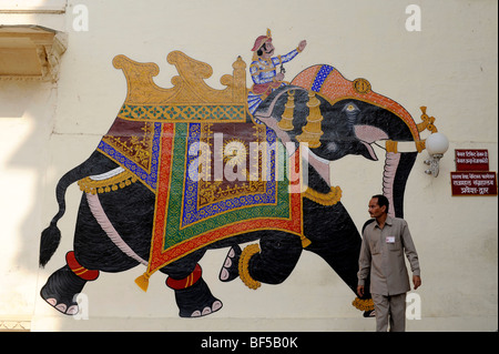 Indian davanti al murale di un elefante con un cavaliere nel palazzo di città, Udaipur, Rajasthan, Nord India, India, Asia del Sud Foto Stock