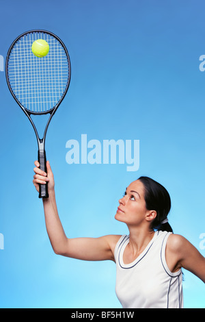 Una donna giocatore di tennis che serve contro uno sfondo blu. Foto Stock