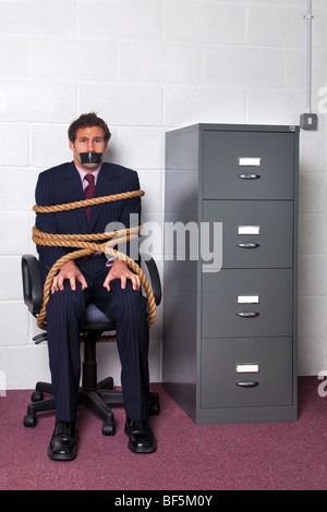 Imprenditore legato ad una sedia da ufficio con la fune, la paura di guardare sul suo volto. Foto Stock