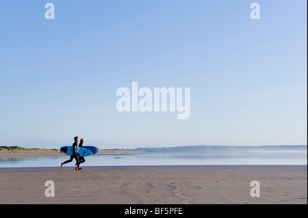 Surfers correre lungo la spiaggia sulla North Devon costa Foto Stock