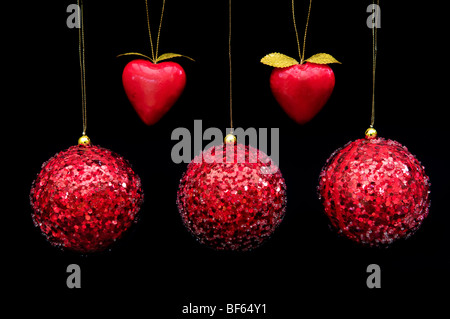 Cinque color rosso baubles decorativi e forme di cuore appeso con filo di oro su sfondo nero Foto Stock