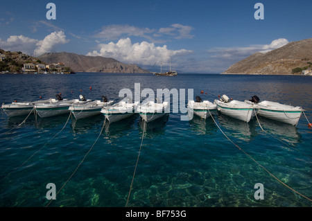 Una fila di otto piccole imbarcazioni ormeggiate nel porto di Symi Town, Grecia. Foto Stock