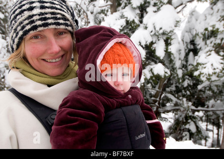 Donna madre con bambino piccolo in un babybjorn camminare in inverno Foto Stock