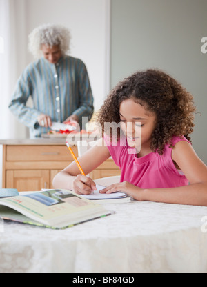 Ragazza facendo compiti a casa con la nonna in background Foto Stock