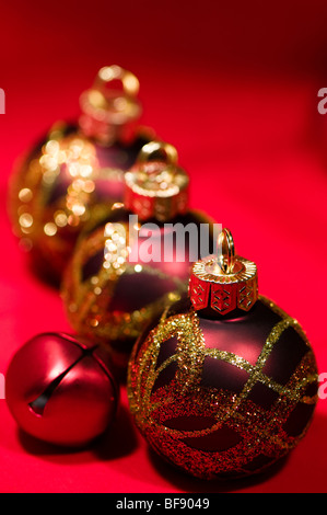 Fila di multi-colore di glittery Christmas baubles contro uno sfondo rosso Foto Stock