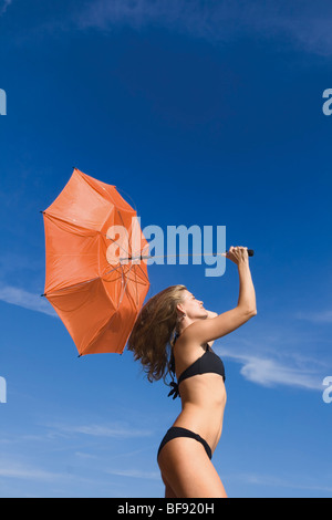 Donna che mantiene all'interno fuori ombrello arancione contro il cielo blu Foto Stock
