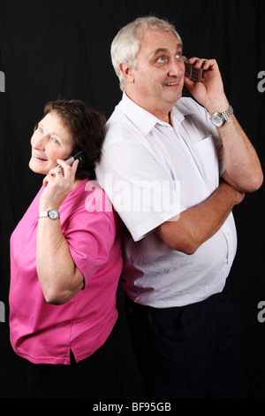 Coppia tardo medio di età compresa tra i coniugi in piedi di schiena chiamando parlando parlando al telefono mobile utilizzando la tecnologia Foto Stock