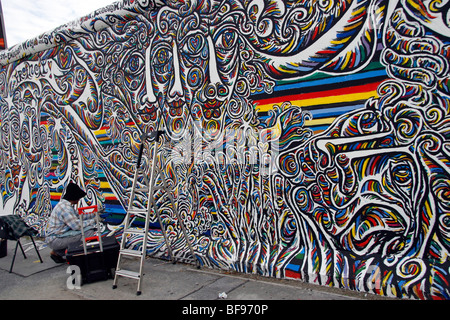 Un artista dipinge il muro di Berlino, all'East Side Gallery, a 1.3km-lungo la sezione della parete vicino al centro di Berlino. Foto Stock