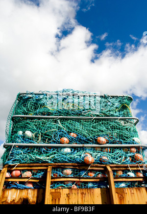 Colorato la pesca commerciale di reti impilate su un rimorchio arrugginito in Dingle Harbour, Dingle, Irlanda contro un cielo blu Foto Stock