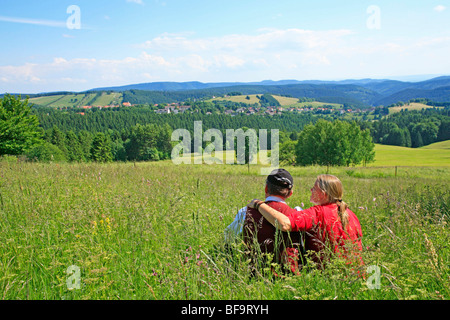 Un giovane seduto in erba alta godendo della vista panoramica di St. Andreasberg, Montagne Harz, Bassa Sassonia, Germania Foto Stock