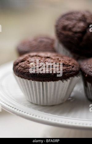 Più appena sfornato muffin al cioccolato su una torta bianca stand Foto Stock