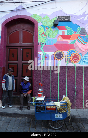 L'uomo vendita di succo di arancia dal carrello nella parte anteriore del negozio di artigianato con il murale sulla parete, Calle Linares, La Paz, Bolivia Foto Stock