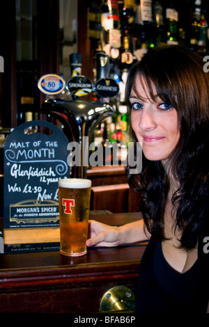 Una bella donna seduto al bar all'interno di un pub scozzese che tiene una pinta di birra scozzese Tennents a Dundee, Regno Unito Foto Stock