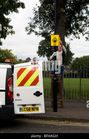 Un consiglio di Lambeth dipendente pende un nuovo quartiere di guardare segno su un Lambeth borough lampada posta a Londra. Foto Stock