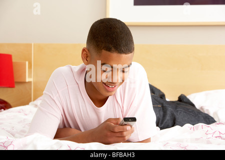 Ragazzo adolescente in camera da letto con telefono mobile Foto Stock