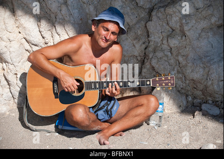 Chitarra giocatore seduto al sole e a suonare la chitarra su un isola greca Foto Stock